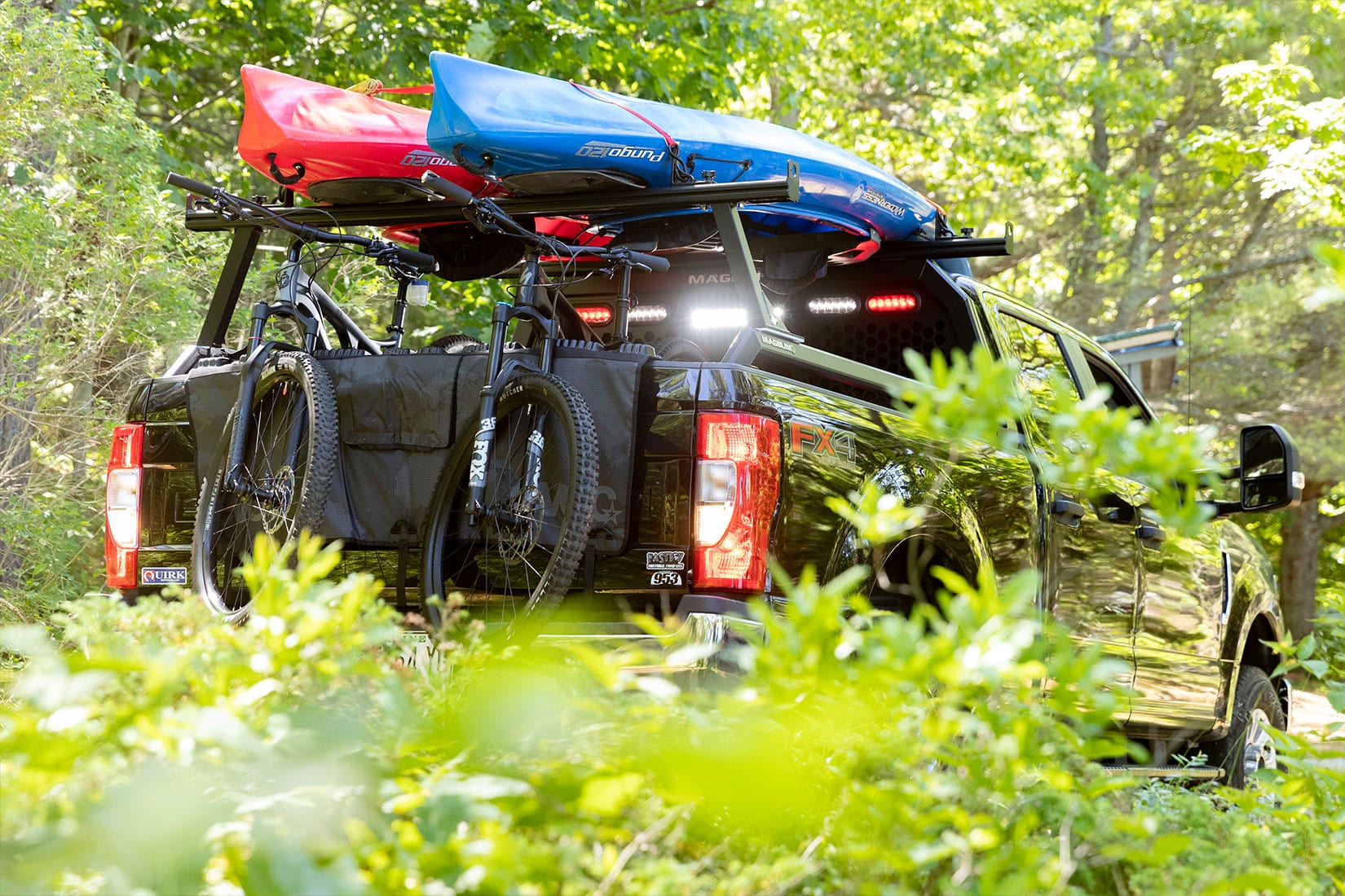 Black pickup truck decked out with a Magnum low pro honeycomb headache rack, bed rails, rear cargo rack - loaded with kayaks driving off-road.