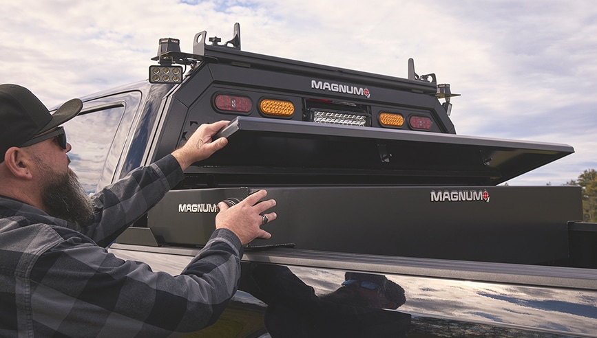 person opening toolbox that is mounted at the front of the truck bed - magnum logo on sides of toolbox